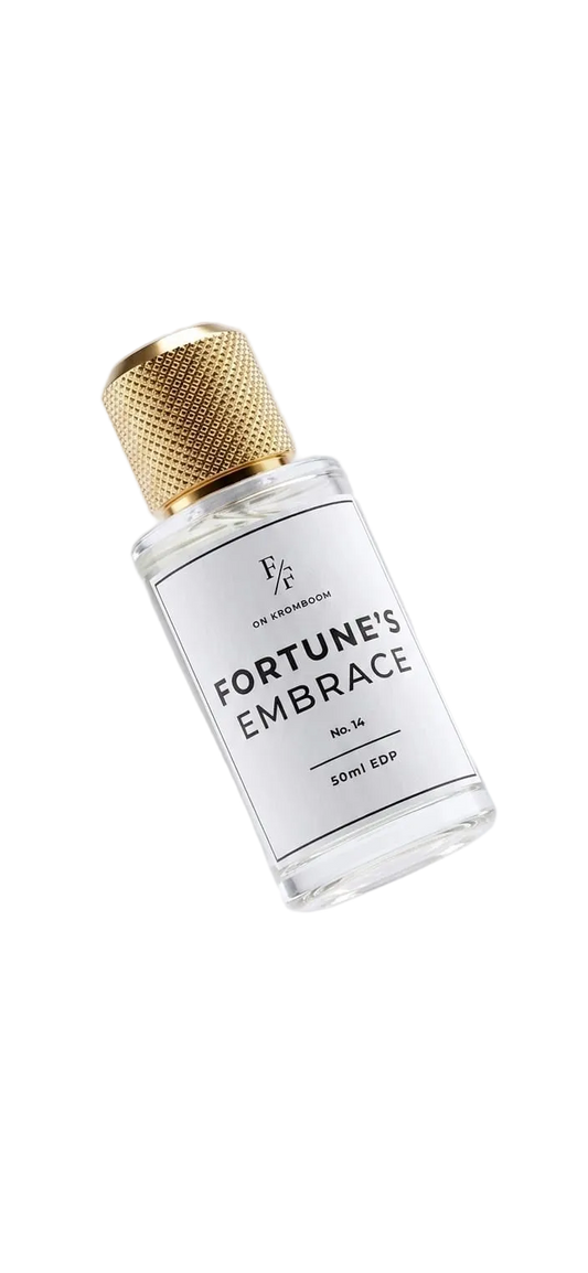 A clear glass bottle of FORTUNE'S EMBRACE cologne by The Alchemist, featuring a textured gold cap and a white label, shown floating against a light gray background.