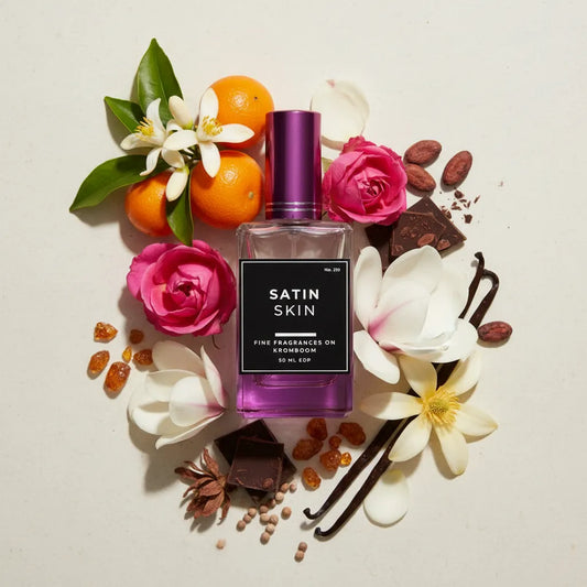 Perfume bottle labeled 'Satin Skin' surrounded by flowers and fruits on a light background